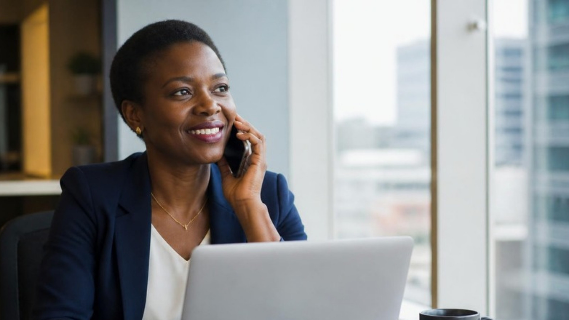Fiscaliste souriante au téléphone avec un client, à son bureau près d'une fenêtre